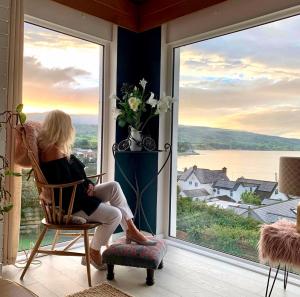 Una mujer sentada en una silla mirando por la ventana en Ballygally Seaview Cottage, en Larne