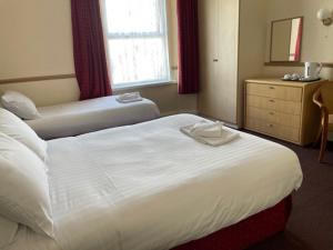 a bedroom with two beds and a dresser and a window at Seascape Hotel in Torquay