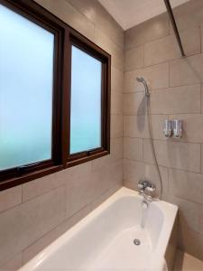 a white bath tub in a bathroom with two windows at Via Renata Prapanca in Jakarta