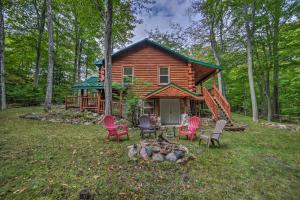 a log cabin in the woods with chairs and a fire pit at Updated Manistique Log Cabin, Yard and Fire Pit in Manistique