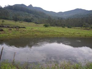 a pond in a field with mountains in the background at Pousada Vó Ciloca in Praia Grande