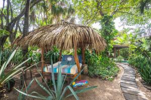 un letto sotto un ombrellone di paglia in un giardino di Sueño del Mar Beachfront Hotel a Tamarindo