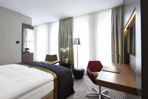 a hotel room with a bed, desk, chair, and lamp at Steigenberger Hotel Am Kanzleramt in Berlin
