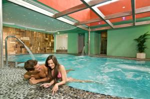 a man and a woman laying in a swimming pool at Hotel Panorama Wellness & Resort in Malosco