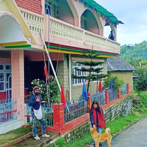 two people standing in front of a house with a dog at Ritu Raj Home Stay & Cafe in Malther