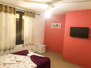 a bedroom with a red wall with a bed and a flat screen tv at Pousada Caminho dos Anjos in Arraial do Cabo
