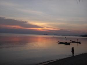 a person standing on the beach with a boat in the water at Neptune's Villa in Haad Rin