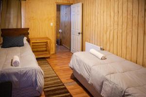 two beds in a room with wooden walls at Hostal Lejana Patagonia in Cochrane