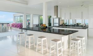 una cocina con armarios blancos y encimera y taburetes negros en Baan Bon Khao - Seaview Private Villa, en Choeng Mon Beach