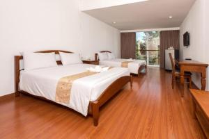 a bedroom with two beds and a desk and a window at Baan Suan Khun Ta and Golf Resort in Ubon Ratchathani