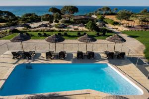 a swimming pool with chairs and umbrellas and the ocean at Vila Alba Resort in Carvoeiro
