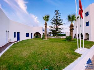 a large white building with palm trees in the yard at Marina Cap Monastir- Appart'Hôtel in Monastir