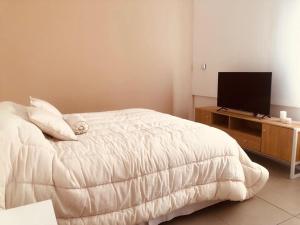 Un dormitorio con una cama blanca y un televisor. en Departamento Altos de Ushuaia, en Ushuaia