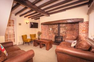 a living room with leather furniture and a brick fireplace at Pear Tree Cottage in Ratton Village