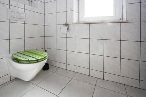 a white tiled bathroom with a toilet with a green seat at Ferienhaus Seeadler am Vilzsee in Mirow in Mirow
