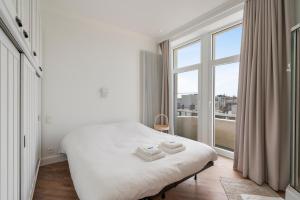 a white bedroom with a bed and a large window at Residence Palace Style app in a unique building in Zeebrugge