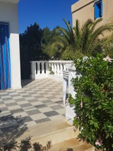 a porch with a checkered floor and a white fence at Maison les Palmiers 300m de la plage in Aghīr
