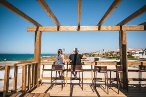 a man and a woman sitting on a deck overlooking the beach at MUTE Hostel Porto Covo in Porto Covo