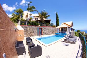 a swimming pool with chairs and a house at Casa da Rainha Bungallow in Estreito da Calheta