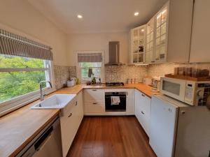 a kitchen with white cabinets and a sink and a microwave at Akarana Cottage in Leura