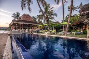 a swimming pool in front of a resort with palm trees at Bali Santi Bungalows in Candidasa