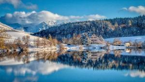 a snowy lake with a house and mountains in the background at Chalet des cascades in Le Mont-Dore
