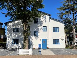 ein weißes Haus mit einem Baum davor in der Unterkunft Dünenkieker Ferienwohnung in Lubmin