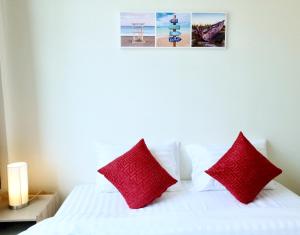 a bedroom with a white bed with red pillows at บ้านคุณพระ แอท โกเตง in Surat Thani