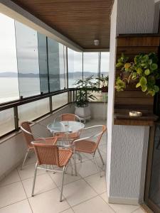 balcón con mesa de cristal y sillas en Cobertura frente ao mar Meia Praia -Itapema -SC, en Itapema
