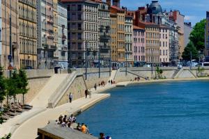 a group of people sitting on a sidewalk next to a river at Appartement La Roseraie PARKING PRIVE in Mâcon
