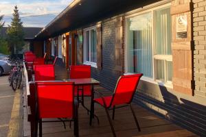 - une rangée de chaises rouges et une table sur une terrasse couverte dans l'établissement Aux Portes du Soleil, à Baie-Saint-Paul