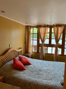 a bedroom with a bed with red pillows and a window at Hostal Corvatsch in San Pedro de Atacama