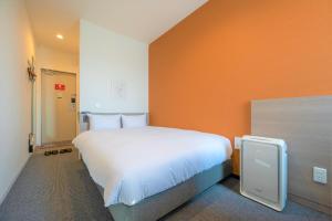 HOTEL R9 The Yard Hitachinaka في Inada: سرير أبيض كبير في غرفة بجدار برتقالي