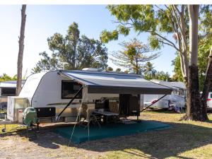 a white rv with a tent and a table and chairs at NRMA Airlie Beach Holiday Park in Airlie Beach