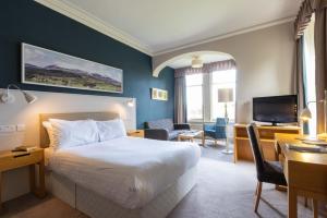 um quarto de hotel com uma cama, uma secretária e uma televisão em The Highland Hotel by Compass Hospitality em Strathpeffer