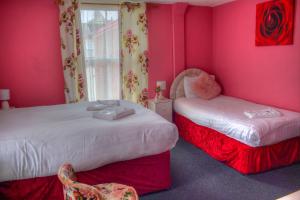 two beds in a room with pink walls and a chair at Villa Rose in Great Yarmouth