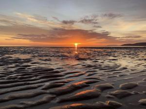 a sunset on a beach with rocks in the water at Bungalow33 Benllech in Benllech