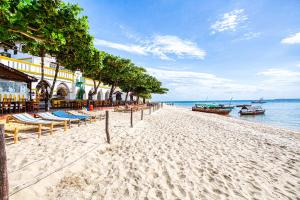 una playa de arena con sillas y barcos en el agua en Tembo House Hotel en Zanzíbar