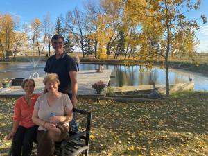 a man and two women sitting on a bench next to a lake at Rolling Hills Country Resort Bed and Breakfast in Three Hills