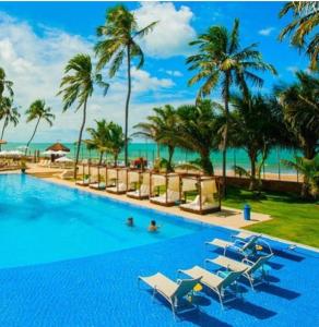 una piscina sulla spiaggia con sedie e palme di JATIÚCA SUITES RESORT - Flat FRENTE MAR a Maceió