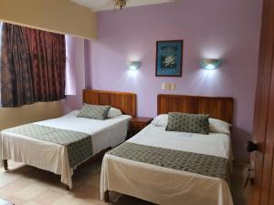 2 camas en una habitación con paredes moradas en Hotel El Faro Malecon en Veracruz