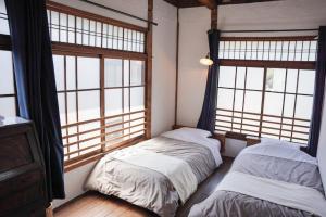 two beds in a room with large windows at Taketa Ekimae Hostel cue in Taketa