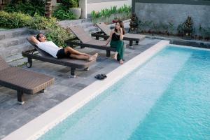 a man and woman sitting on chairs next to a swimming pool at Musa Canggu in Canggu
