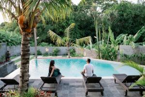 a man and woman sitting next to a swimming pool at Musa Canggu in Canggu