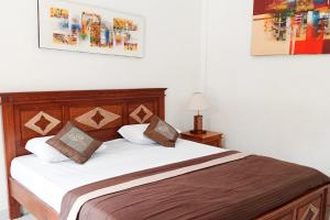 um quarto com uma cama com lençóis brancos e almofadas castanhas em Umah Dauh Homestay em Ubud