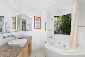 Baño blanco con bañera y lavamanos en Meridien Beachfront Apartments at Trinity Beach, en Trinity Beach