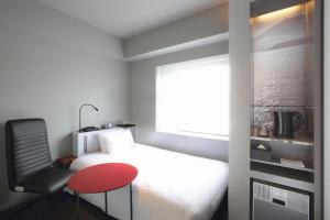 a bedroom with a bed and a chair and a red stool at remm Kagoshima in Kagoshima