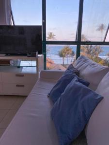 Marulhos Resort Flat Vista Mar في بورتو دي غالينهاس: سرير بمخدات زرقاء وتلفزيون في الغرفة