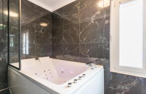 baño de azulejos negros con bañera y ventana en L'étoile et le Merveilleux 2 appartements SPA en Dijon
