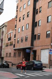 uma mulher a atravessar uma rua em frente a um edifício de tijolos em Hostal Cuzco em Salamanca